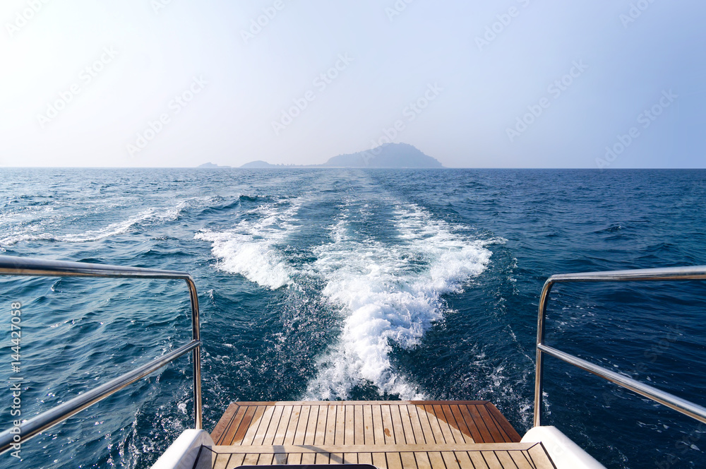 Trace of a wave with foam on the sea behind the boat. Wooden platform and metal handrails on a boat 