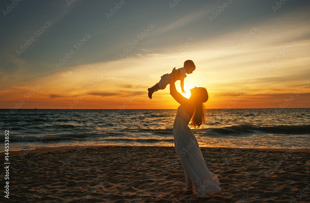 happy family mother with baby son walks by ocean on beach in summer