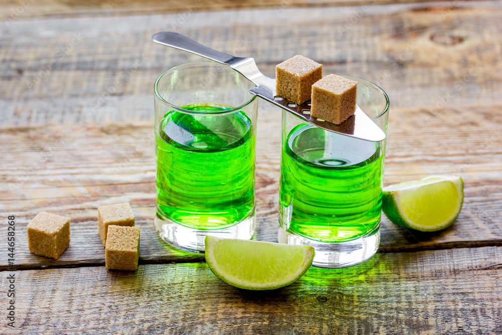 absinthe shots with lime slices and sugar on wooden table background