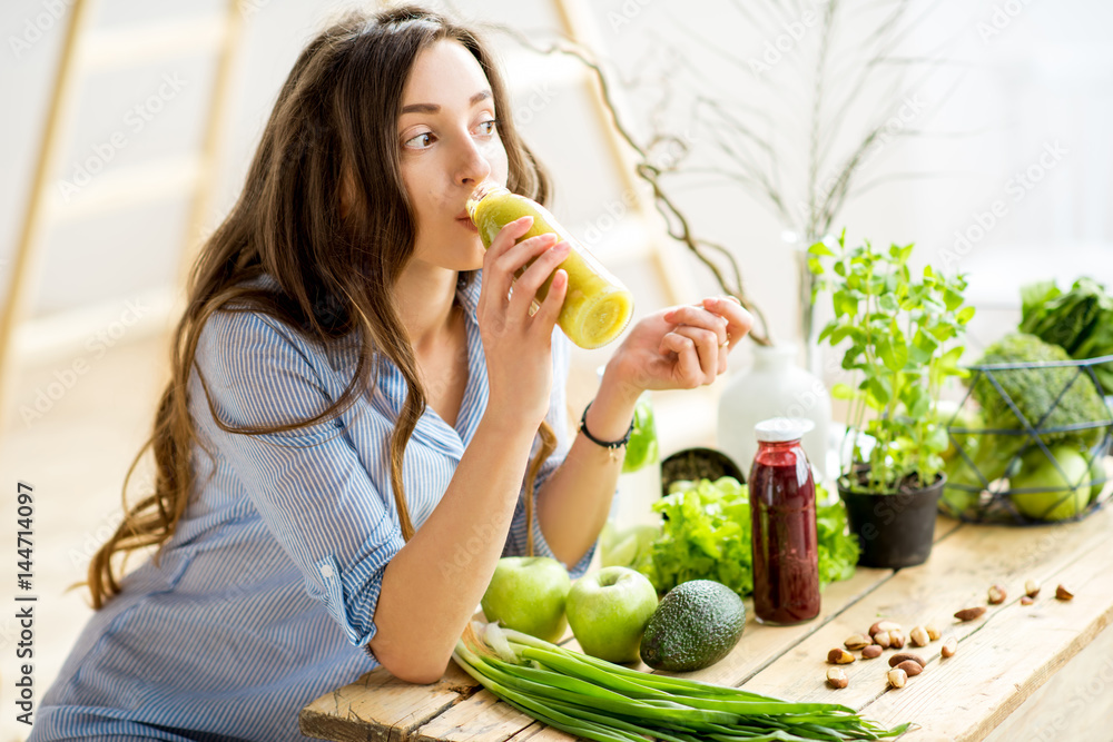 Beautiful woman sitting with healthy green food and drinking smoothie at home. Vegan meal and detox 