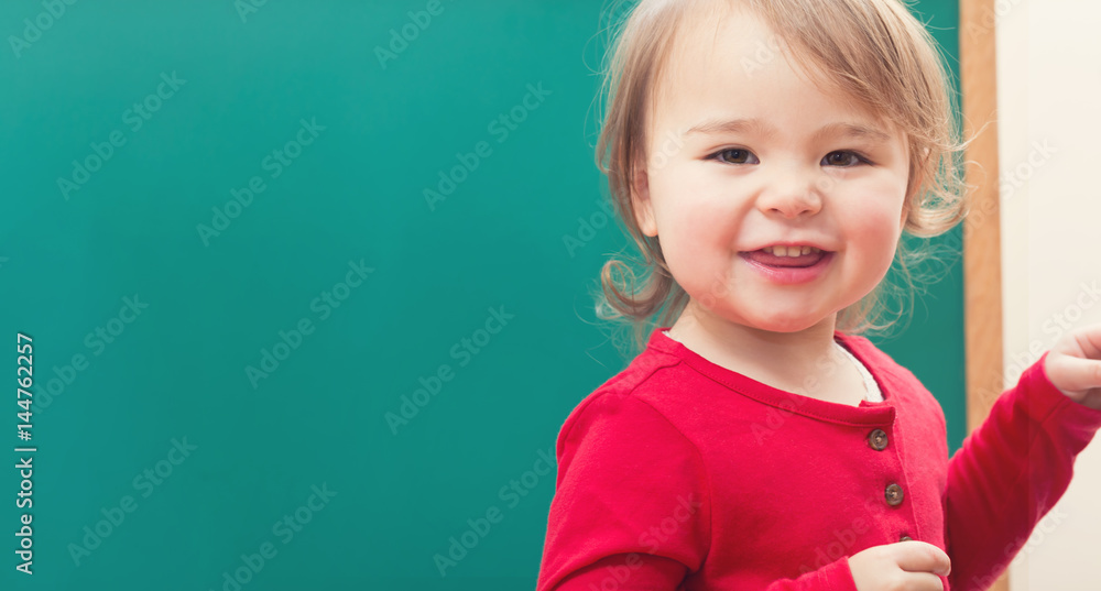 Happy toddler girl smiling in front of a chalkboard