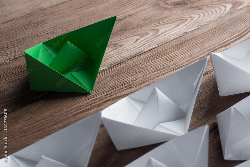 Business leadership concept with white and color paper boats on wooden table