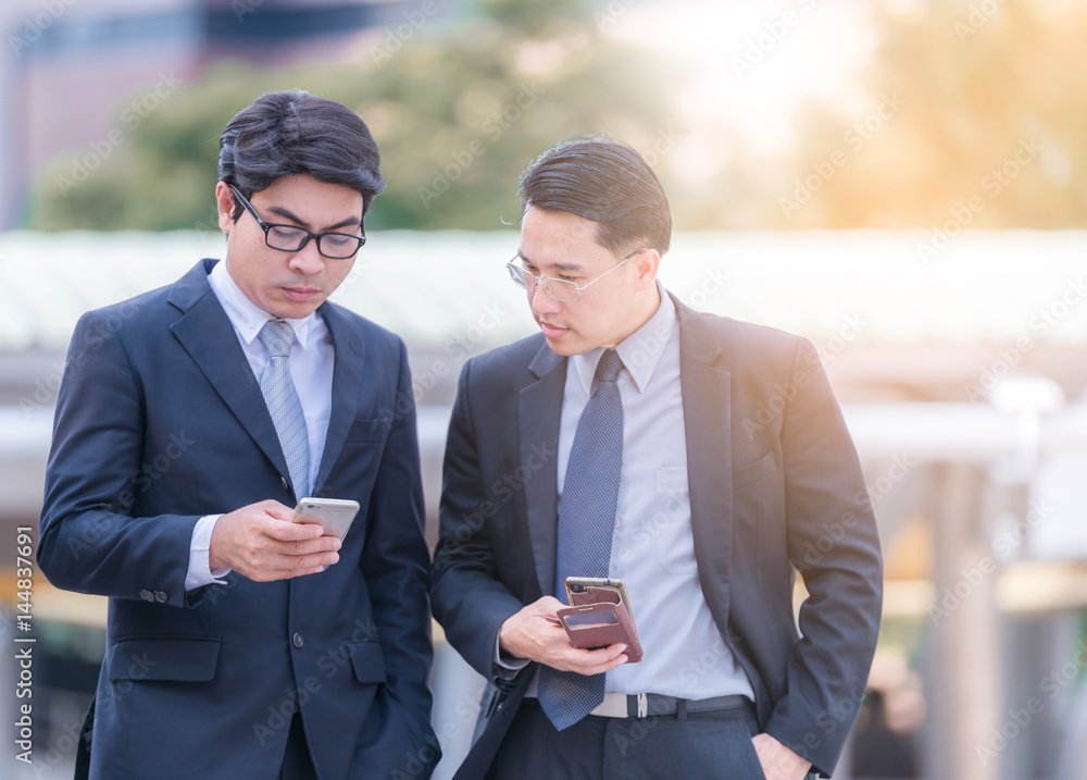 Half length of two young bearded modern businessman using smart phone handhold looking downward the 