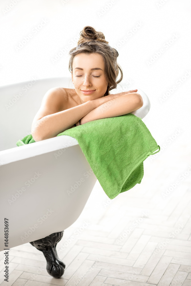 Beautiful young woman relaxing lying in the retro bathtube in the white bathroom