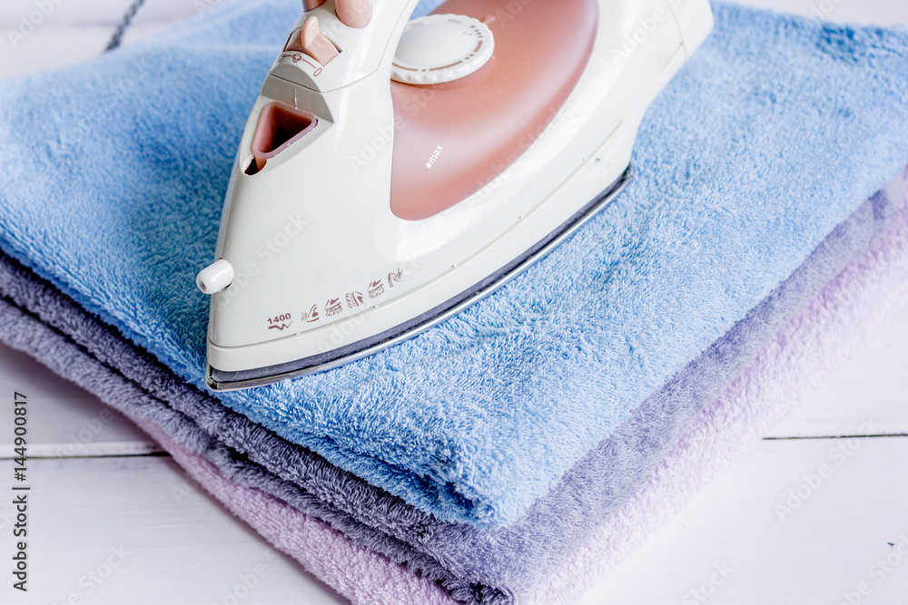 Pile of colorful towels with iron in laundry wooden background