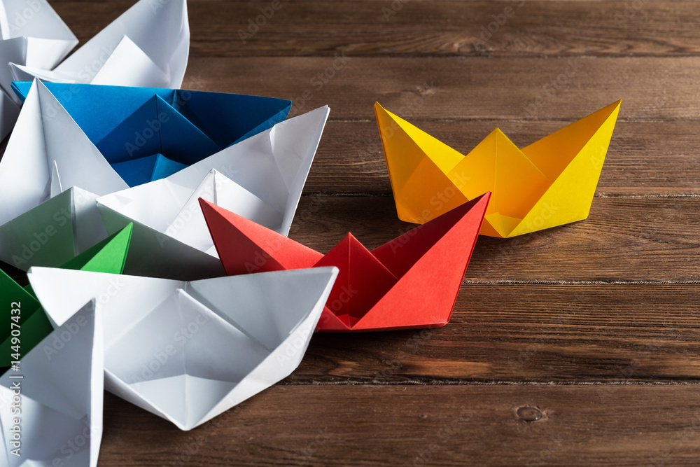 Business leadership concept with white and color paper boats on wooden table