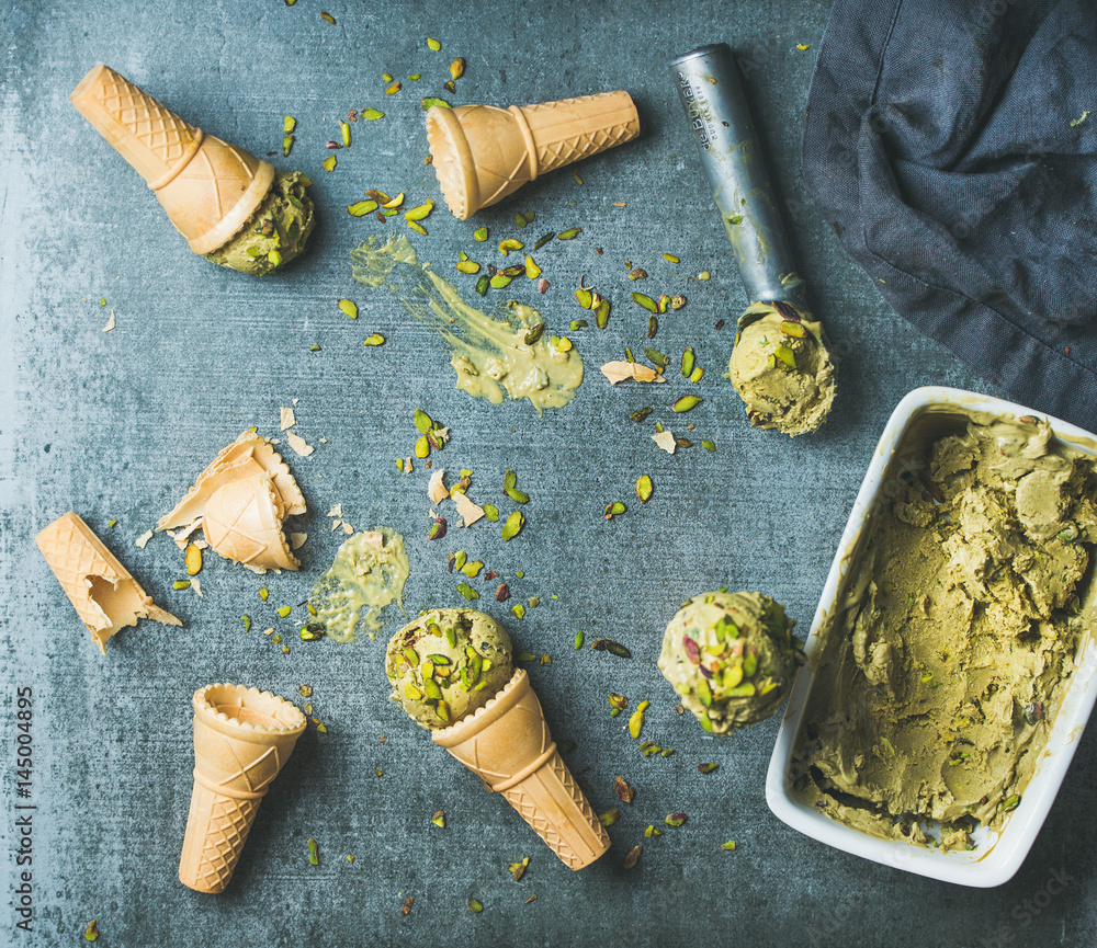 Homemade pistachio ice cream in ceramic mold and metal scooper with crashed pistachio nuts and waffl