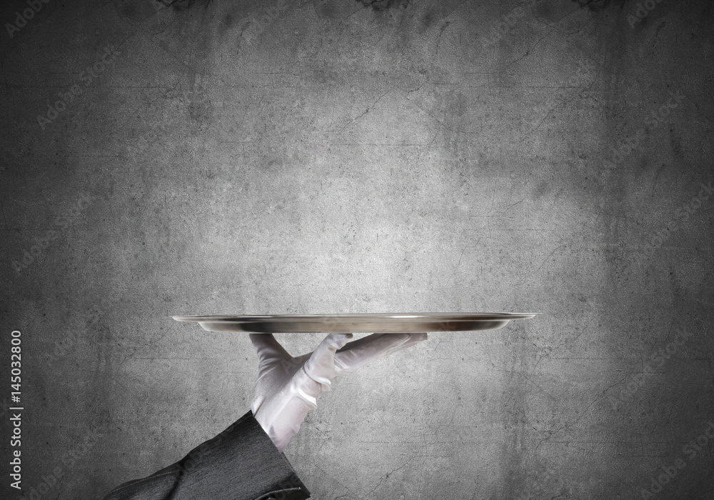 Hand of butler holding empty metal tray against concrete background