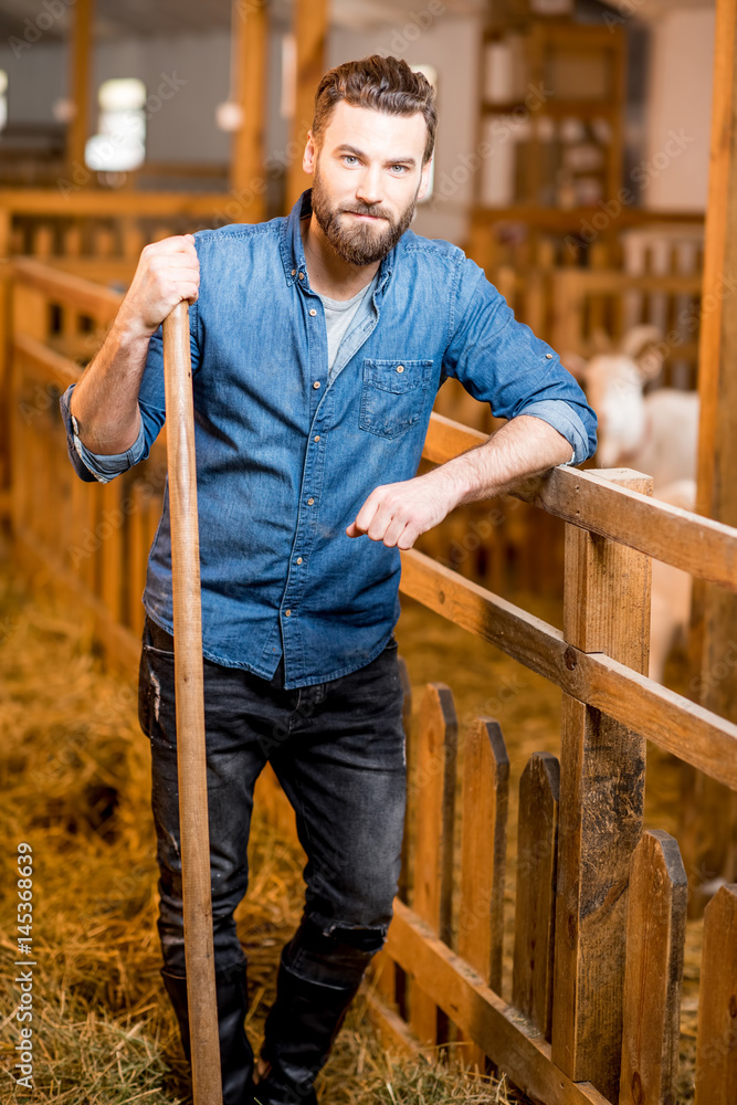 Portrait of a handsome farmer standing with fork at the goat barn. Natural milk production and farmi