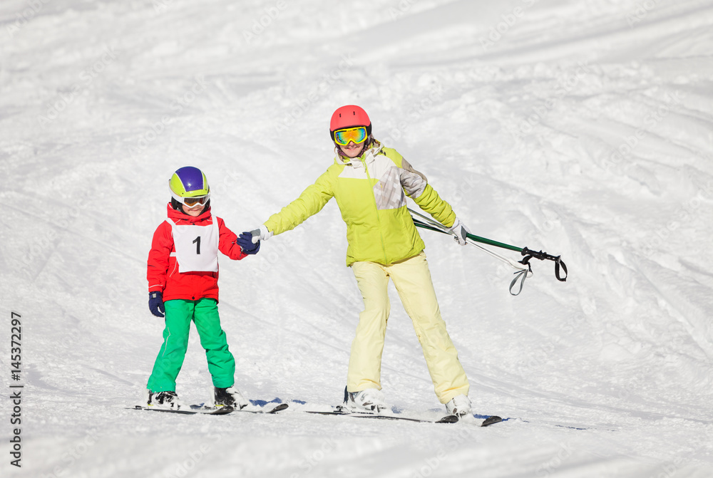 Active mother teaching son skiing holding hands