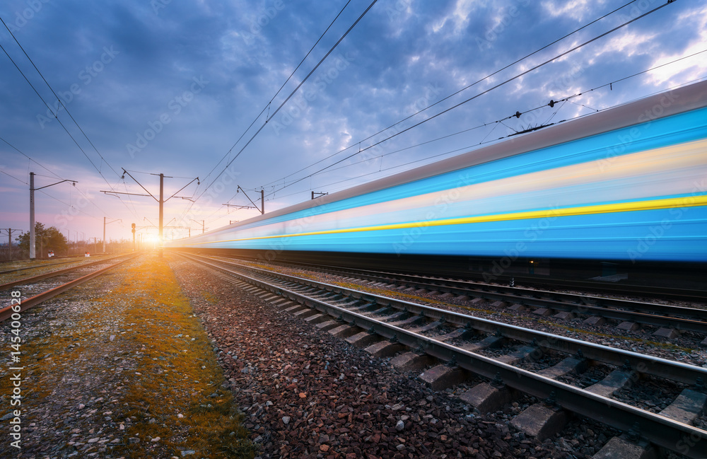 High speed blue passenger train in motion on railroad track at sunset. Blurred modern train. Railway