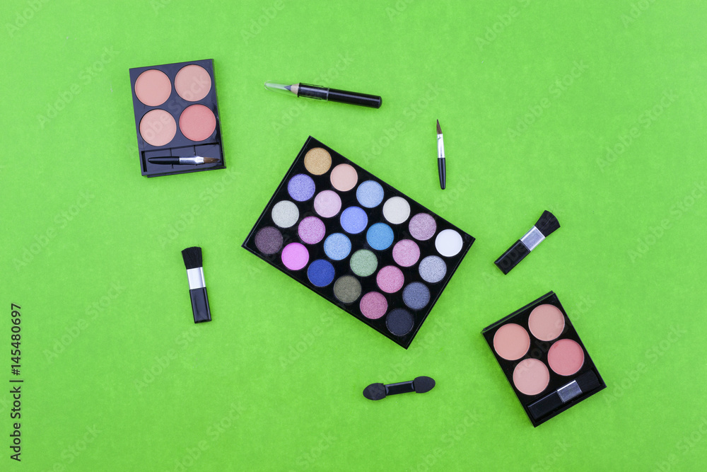 Flat lay photo of various makeup brush, eyeshadow and cosmetics on colorful paper background.