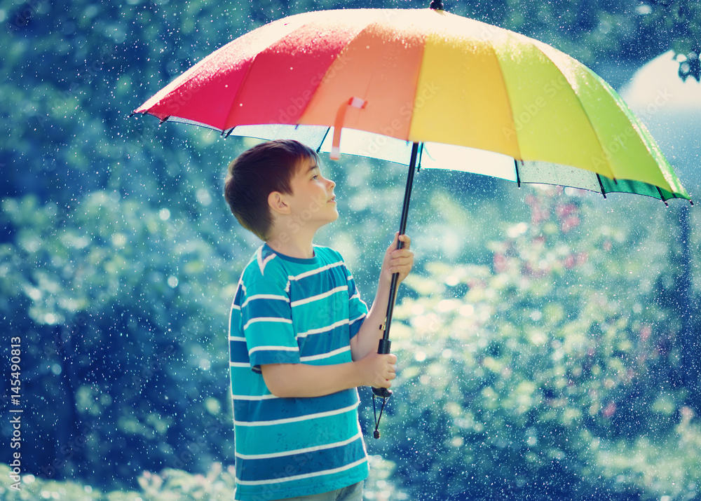 Child on rainy weather. Boy holding colourful umbrella under rain in summer