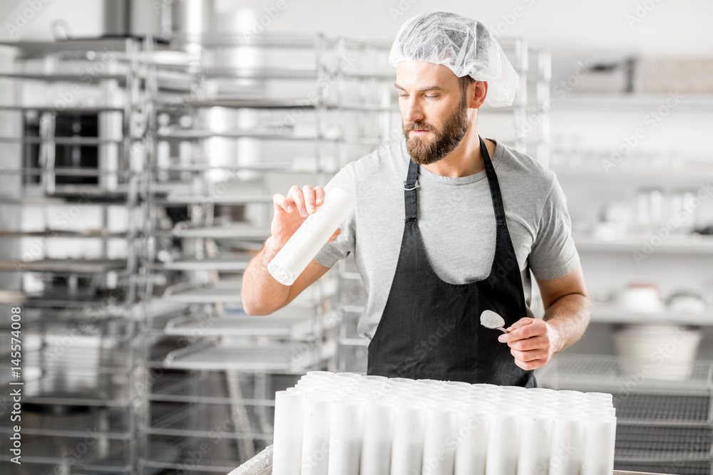 Handsome cheese maker checking quality of a cheese working at the small producing farm