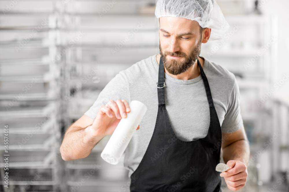 Handsome cheese maker checking quality of a cheese working at the small producing farm