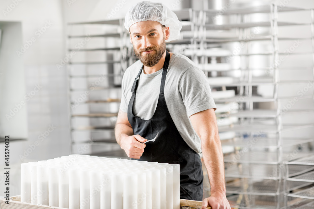 Portrait of a handsome cheese maker in uniform forming cheese into molds at the small producing farm