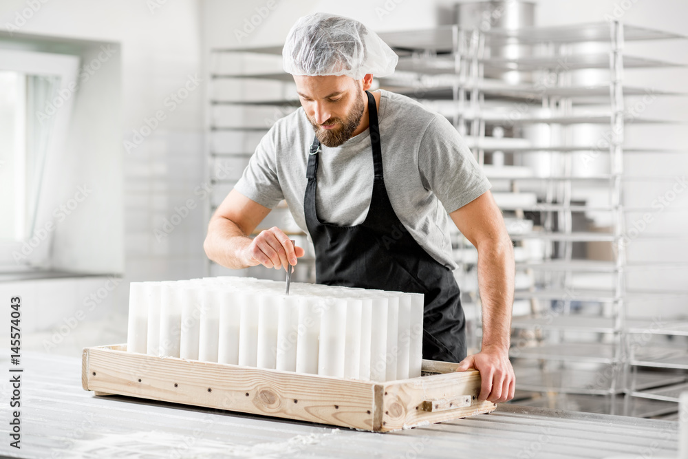 Handsome cheese maker in uniform forming cheese into molds at the small producing farm