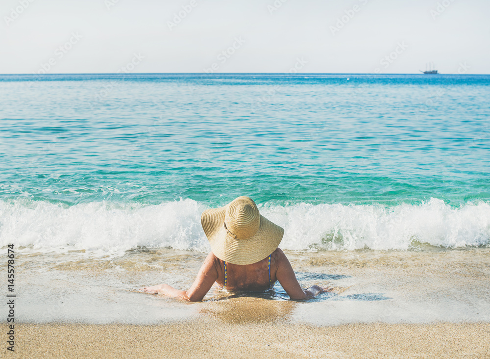 Beautiful slim senior woman tourist in bikini and hat lying on sand enjoying sea at Meditteranean re