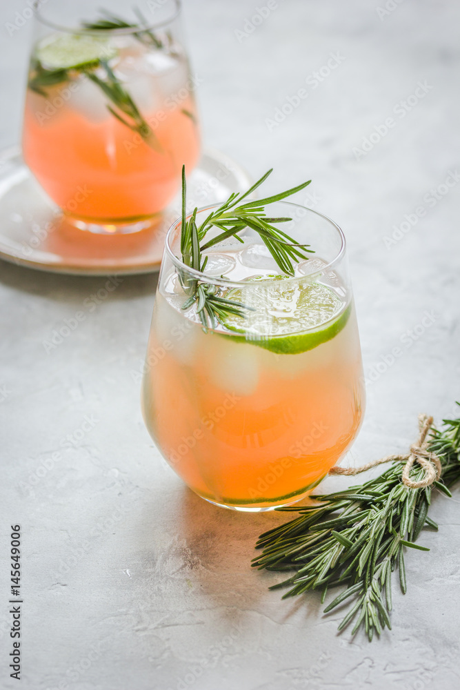 sliced lime, rosemary and natural juice in glass on stone table background