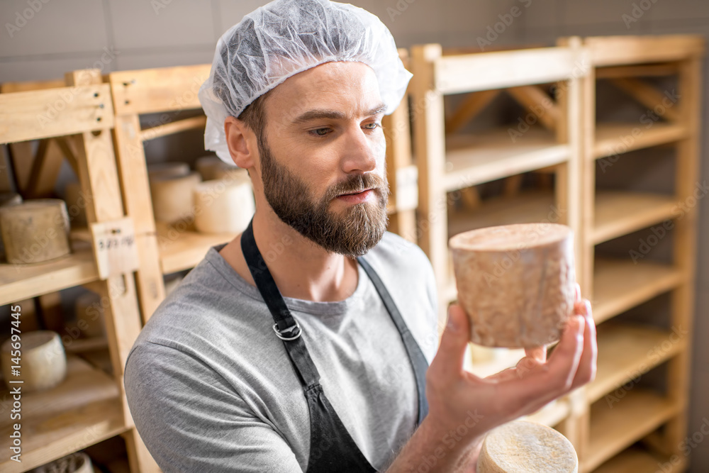 Handsome cheese maker checking the aging process of the goat cheese standing at the small cellar