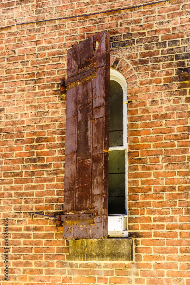 Very old semi-closed shutter with rust old window on a brick building