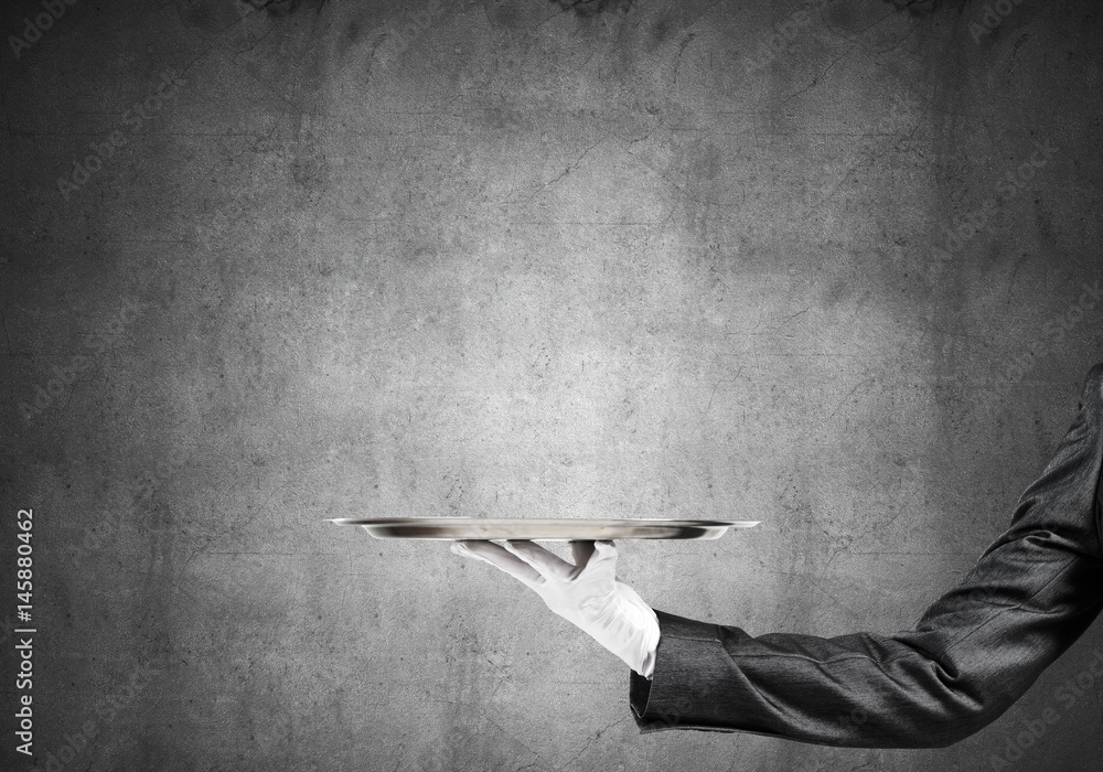 Hand of butler holding empty metal tray against concrete background