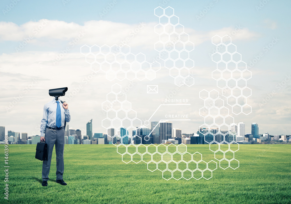 Camera headed man standing on green grass against modern citysca