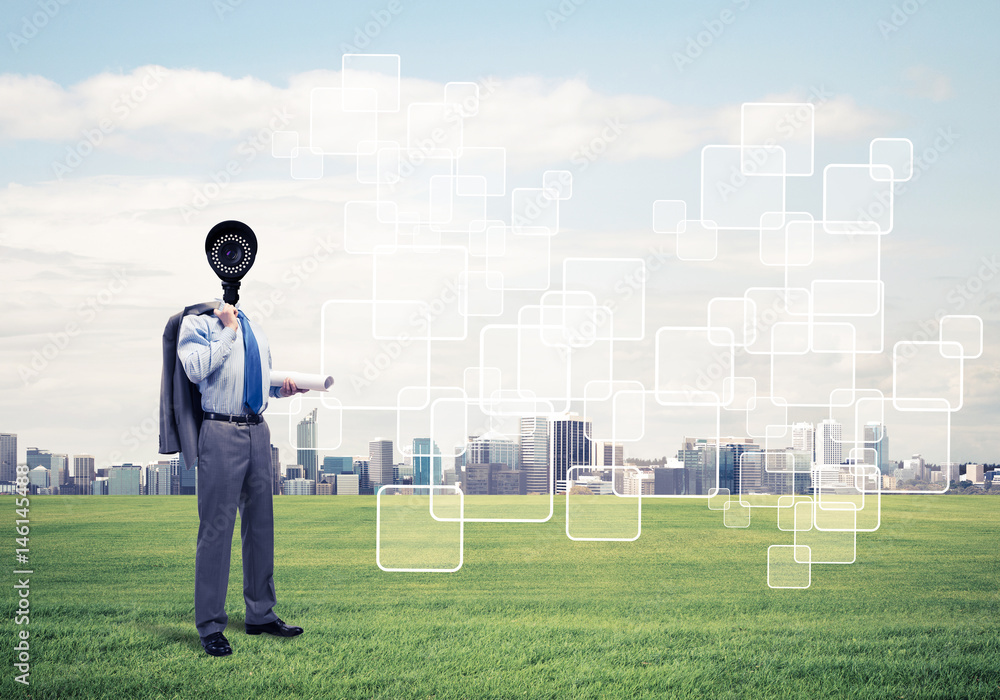 Camera headed man standing on green grass against modern citysca