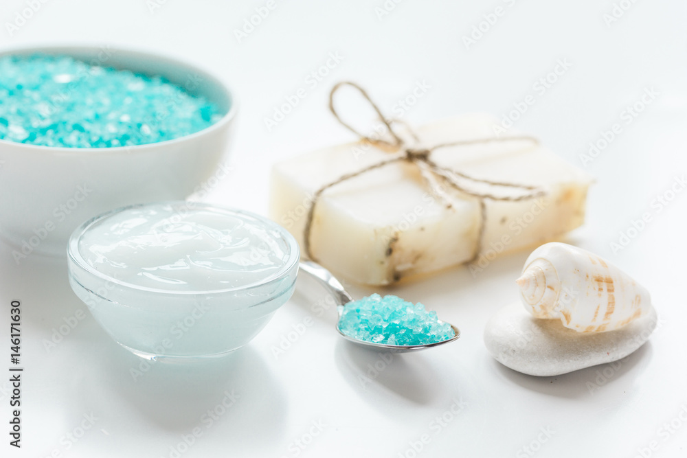 blue bath salt, body cream and shells for spa on white table background