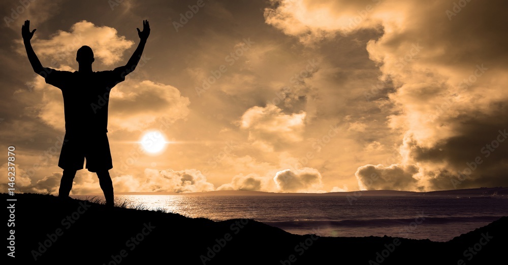 Silhouette sportsman with arms raised at beach during sunset