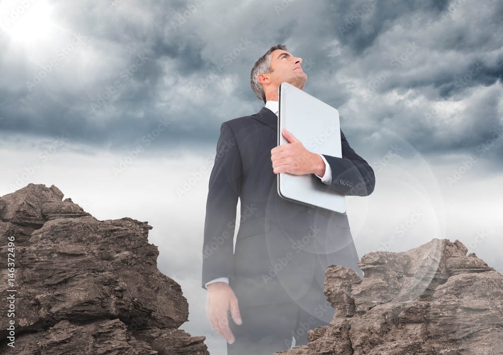 Business man with laptop and flare looking up behind rocks