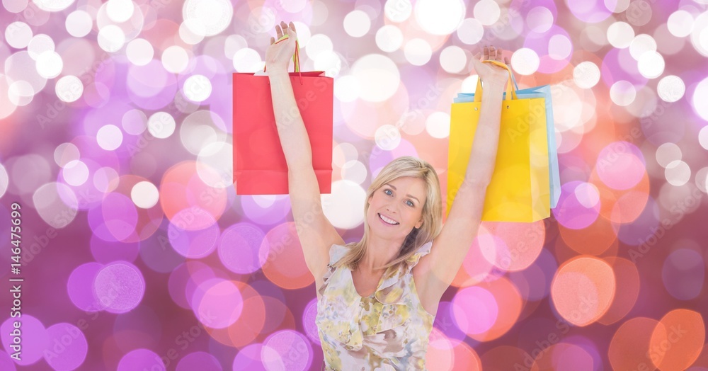 Happy woman with arms raised carrying shopping bags over bokeh