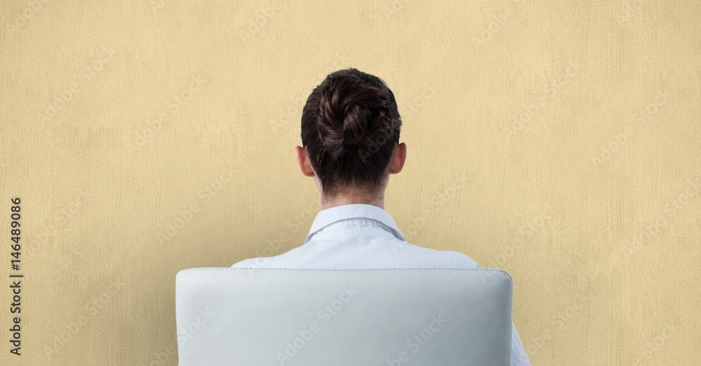 Rear view of businesswoman sitting on chair against wall