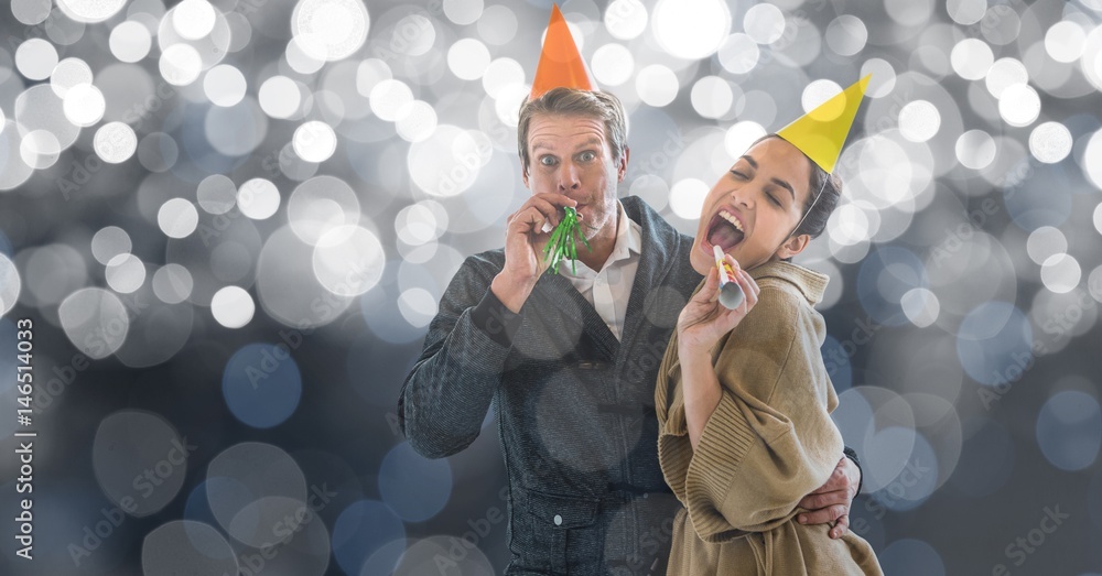 Happy couple blowing party horns against blur background