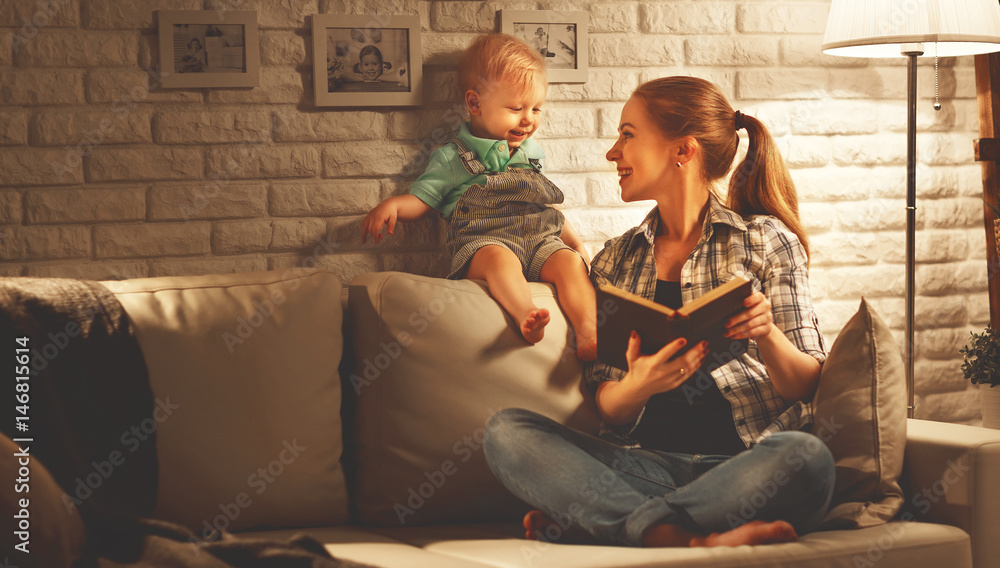 Family before going to bed mother reads to her baby son book near a lamp in the evening.