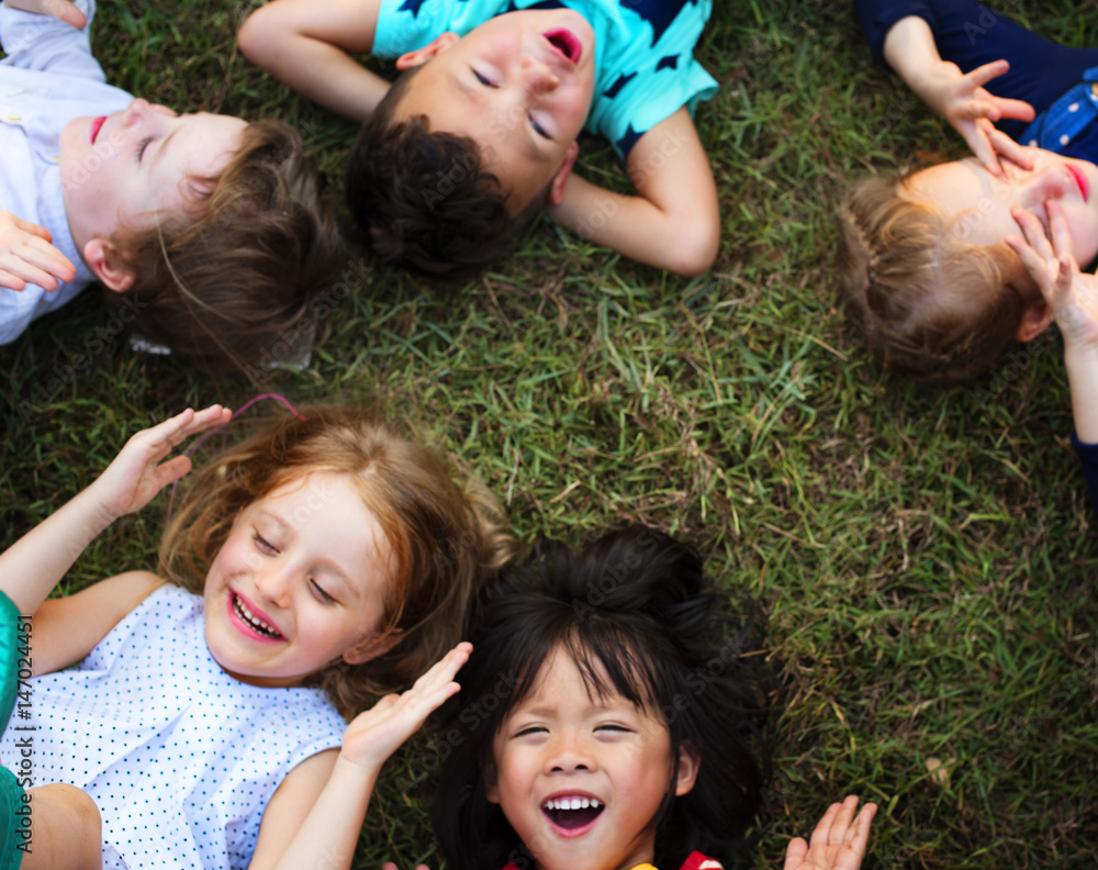 Group of kindergarten kids lying on the grass at park and relax with smiling