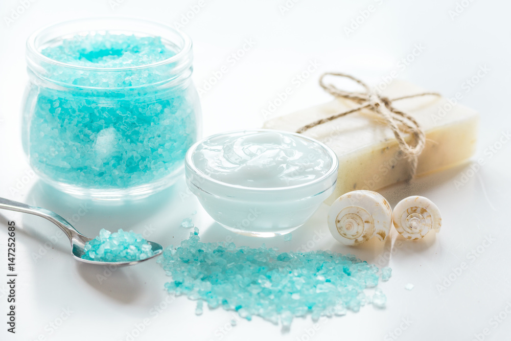 blue bath salt, body cream and shells for spa on white table background