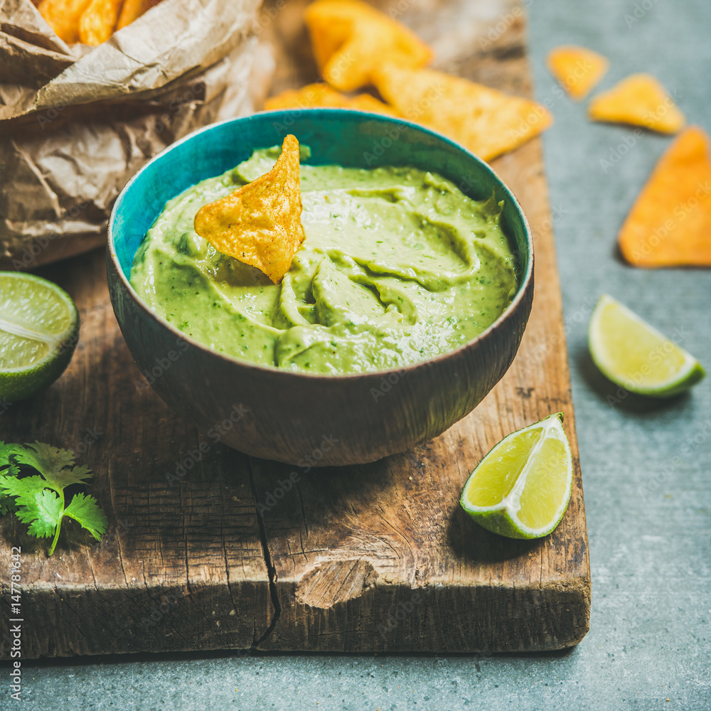 Fresh guacamole sauce in blue bowl, mexican corn chips, glass of wheat beer on rustic wooden serving