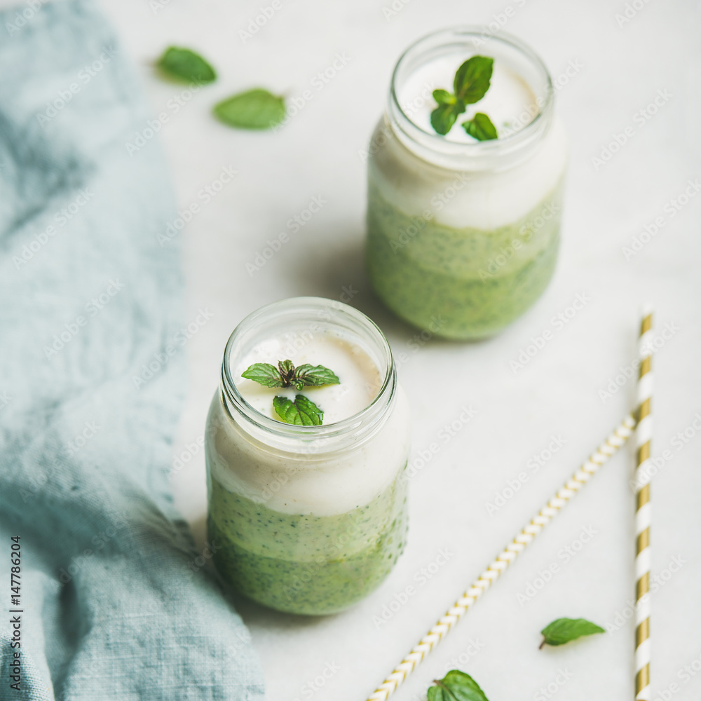 Ombre layered green smoothies with mint in glass jars over light grey background, selective focus, s