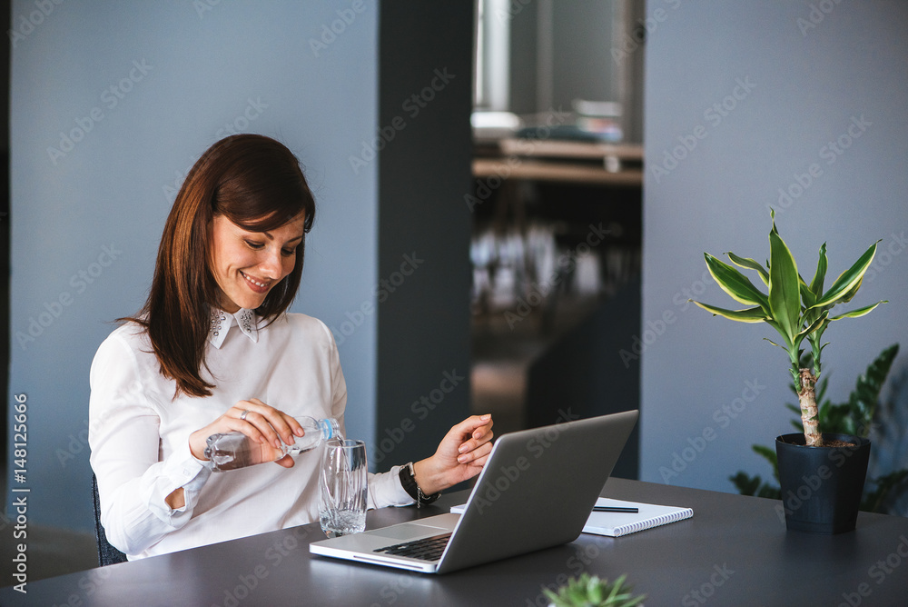 Stay hydrated. Pretty young woman in the office drinking water while working.