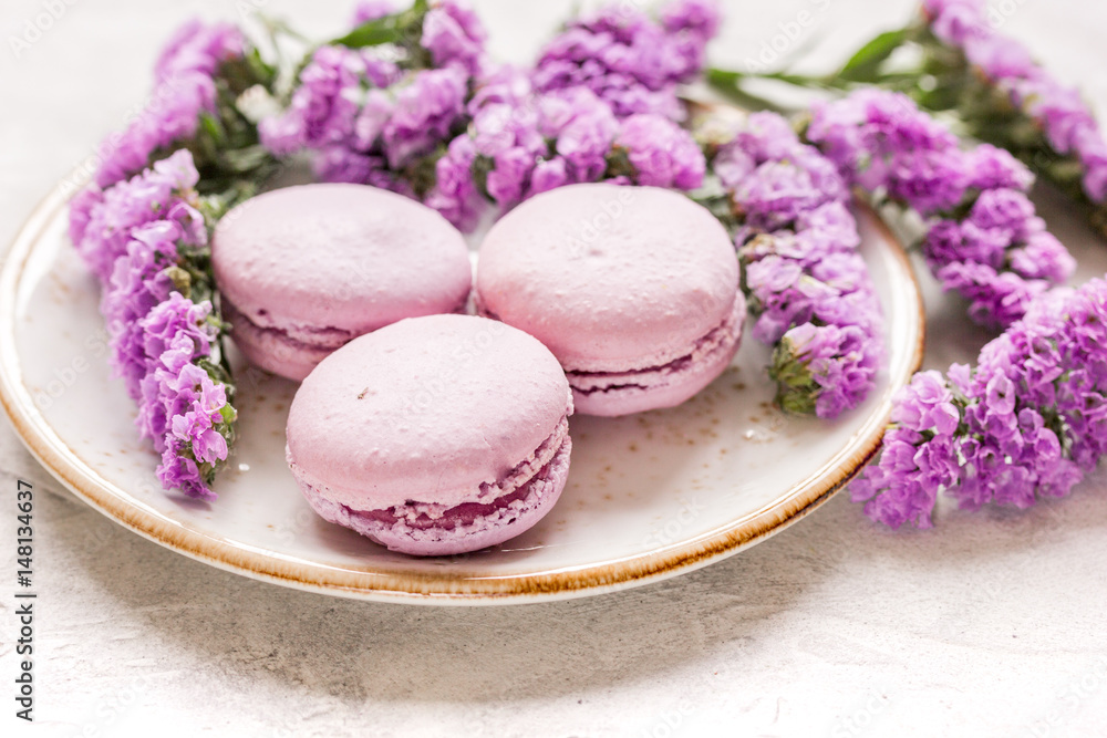 macaroons and mauve flowers for light breakfast on white desk background