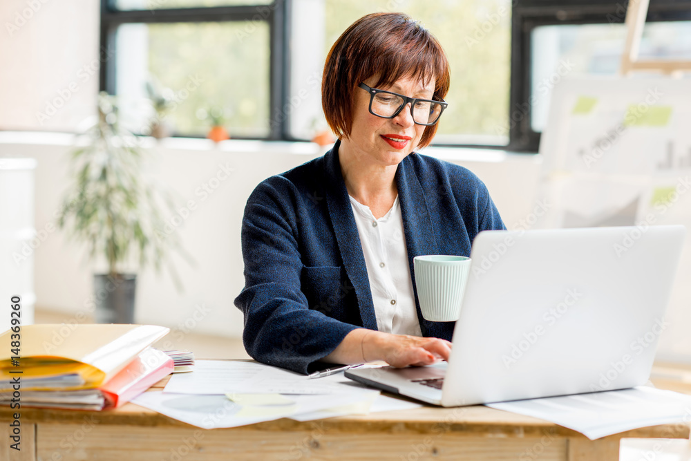 Portrait of a senior businesswoman working with documents and laptop at the bright modern office int