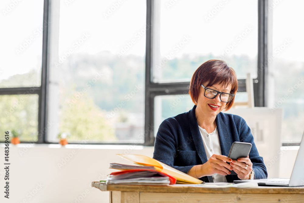 Senior businesswoman working with documents and smartphone at the bright modern office interior