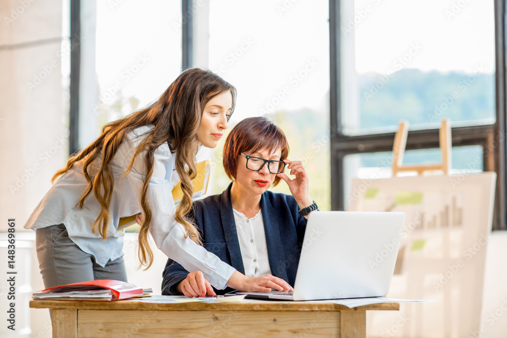 Young and older businesswomen working together on documents at the modern office interior