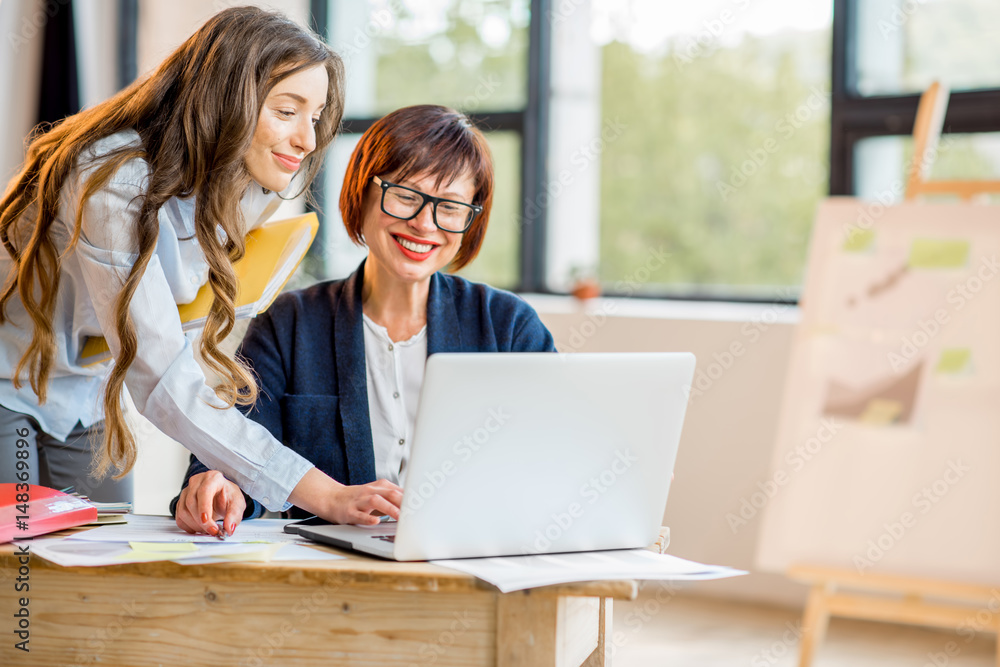 Young and older businesswomen working together on documents at the modern office interior