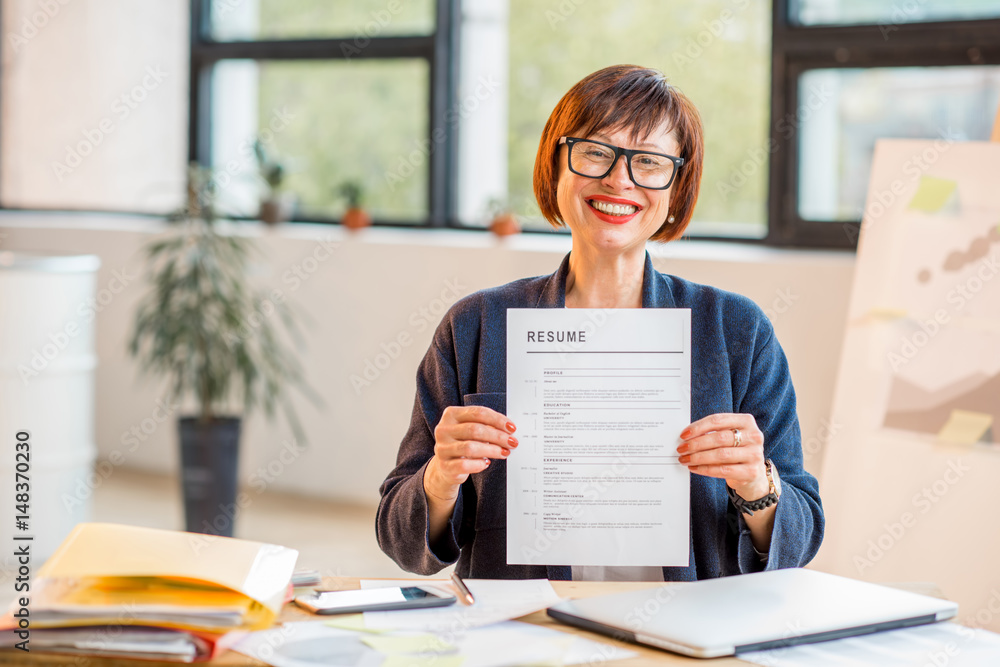 Elegant older woman holding resume document sitting at the modern office