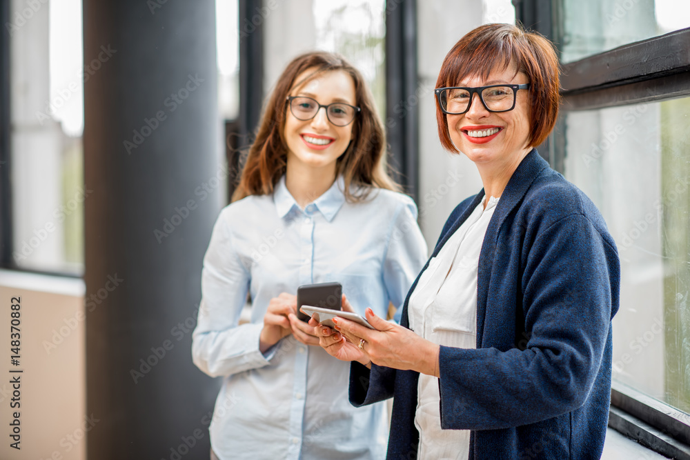 一位年轻和年长的女商人站在办公室窗户附近的肖像