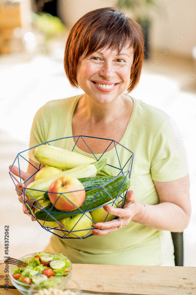 Smiling older woman holding fruits and vegetables indoors