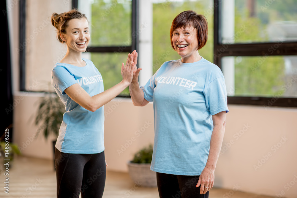 Portrait of an older and young female volunteers in blue t-shirts standing together at the office