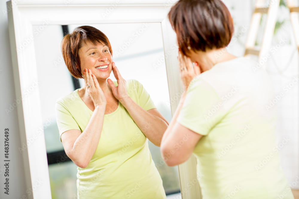 Beautiful older woman looking at her face with a smile into the mirror